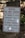 A warning sign is placed outdoors against a background of stone steps and walls, surrounded by some greenery. The sign indicates that the building is vacant and unauthorized entry is prohibited. Contact information for further inquiries is provided at the bottom.