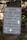 A warning sign is placed outdoors against a background of stone steps and walls, surrounded by some greenery. The sign indicates that the building is vacant and unauthorized entry is prohibited. Contact information for further inquiries is provided at the bottom.