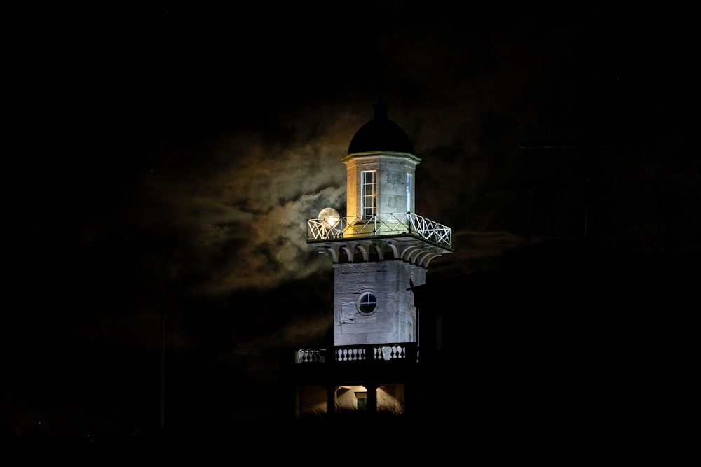 Una torre de reloj iluminada por la noche con la luna de fondo