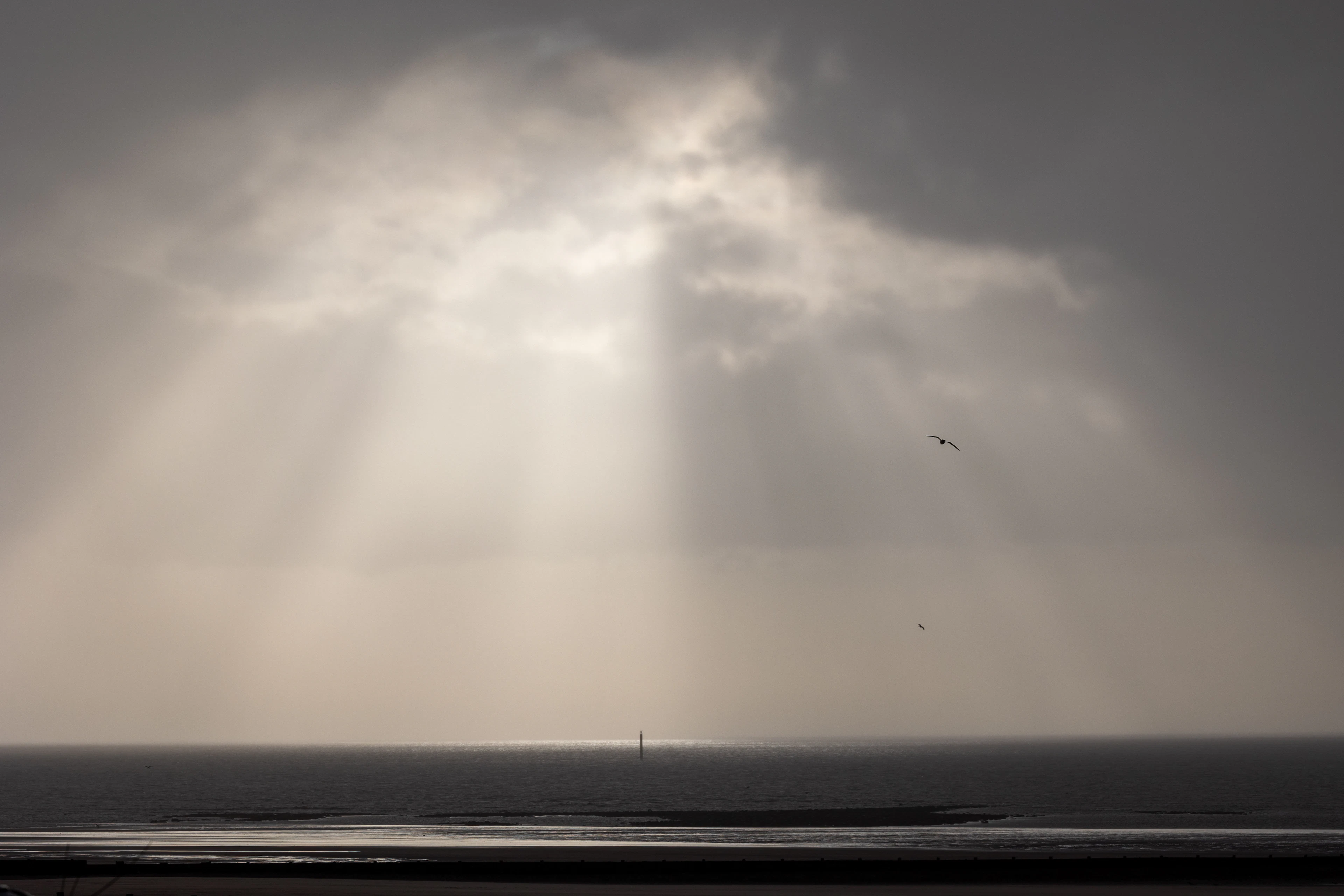 Sunlight streaming through heavy storm clouds over the sea