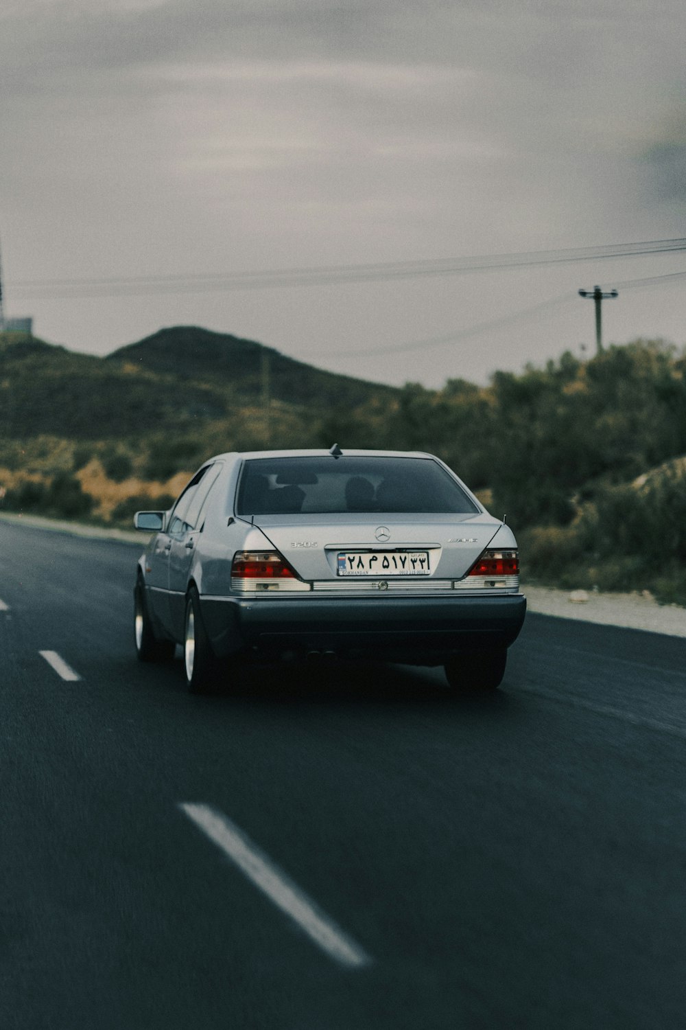 a silver car driving down a road next to a hill