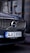 A close-up view of the front grille of a Volvo car, prominently displaying the brand's emblem. The car has a Turkish license plate, and a reflection of a person wearing a hard hat is visible in the background.