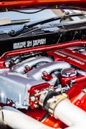 A close-up view of a car engine featuring prominently the words 'Made in Japan' and 'Twin Turbo'. The engine components are detailed, with visible pipes, bolts, and metal surfaces. The colors red and silver are dominant in the design, indicating performance and craftsmanship.