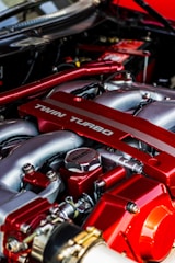 Close-up view of a high-performance car engine featuring a prominent red-tinted twin turbo system with metallic components and intricate detailing.