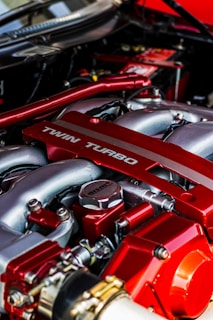 Close-up view of a high-performance car engine featuring a prominent red-tinted twin turbo system with metallic components and intricate detailing.