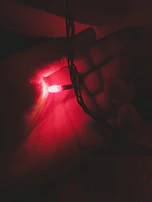 Hands holding a wellness device emitting a gentle 528hz frequency light in a dimly lit room.