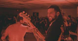 Guitarist strumming with a big smile while the audience claps along in a cozy venue.