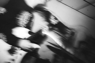 A blurred black and white photograph capturing dynamic motion, possibly of a guitarist in action on stage, creating an abstract and intense visual effect.