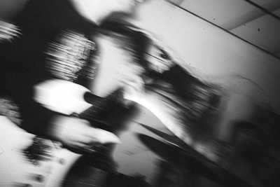 A blurred black and white photograph capturing dynamic motion, possibly of a guitarist in action on stage, creating an abstract and intense visual effect.