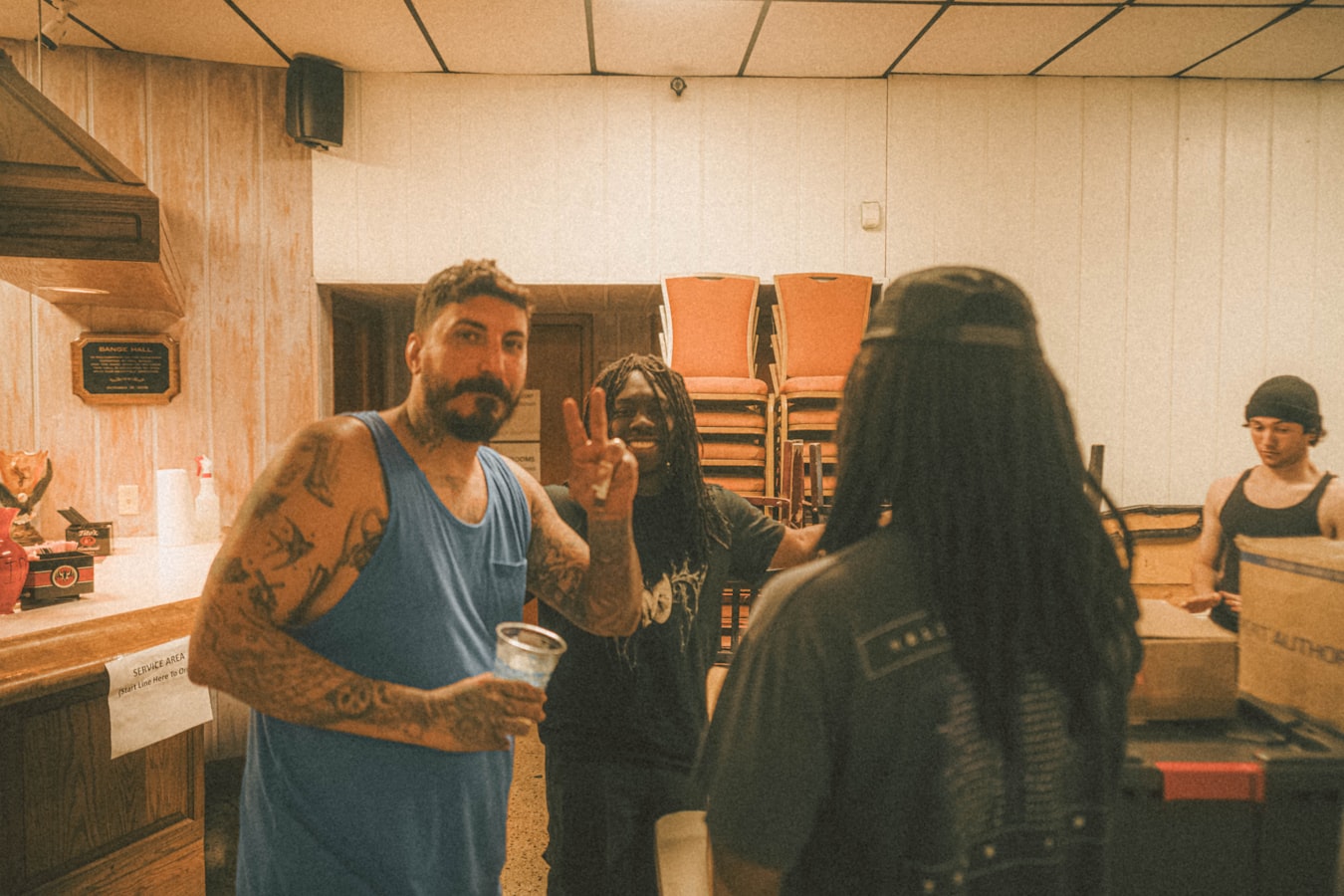 A group of travelers gathered in a hostel kitchen at night, mid-conversation around a shared table