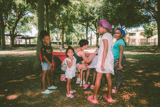 A woman teaching children under a large tree, with bright smiles and attentive faces.