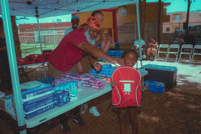 A smiling child holding a backpack filled with school supplies at a community event.