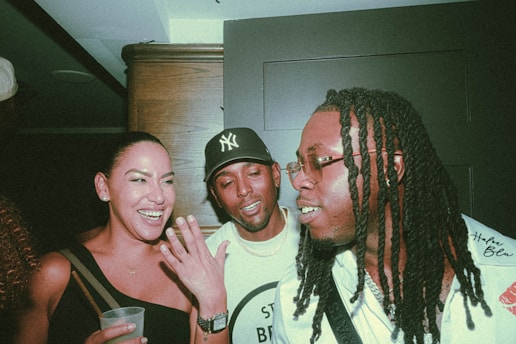 Three longtime friends laughing together in a cozy Buffalo living room, microphones set up for their podcast.