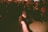 A person wearing a cap and dark clothing is energetically dancing in a dimly lit room filled with a crowd. The crowd watches attentively, with some capturing the moment or cheering. The lighting creates dramatic shadows, enhancing the dynamic and vibrant atmosphere.