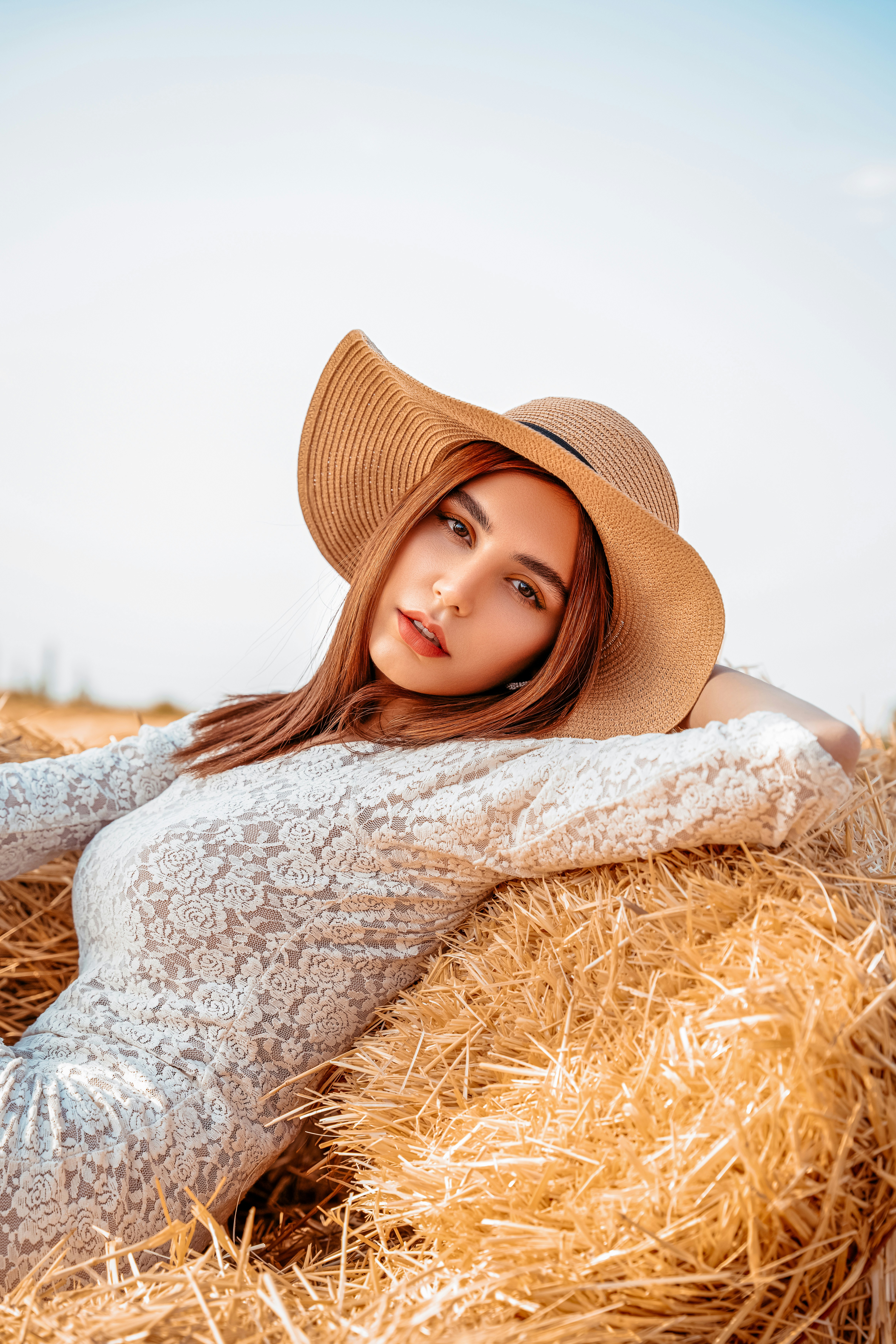 a woman wearing a hat laying on a pile of hay