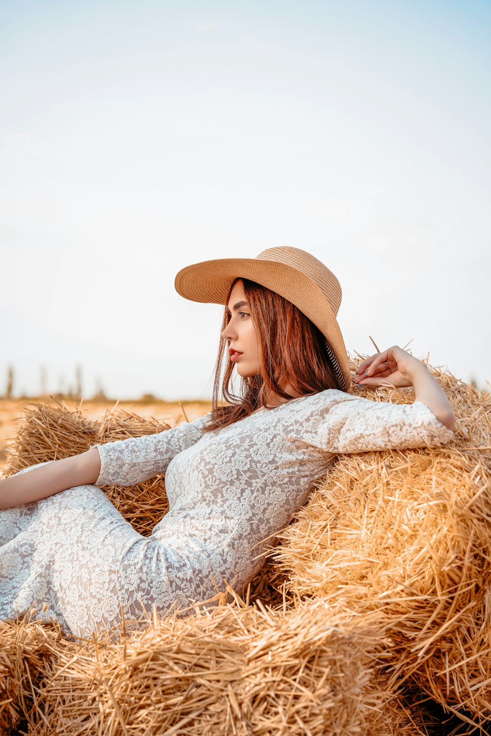a woman in a hat laying on a bale of hay