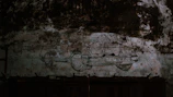A faded mural peeling off a crumbling wall in an abandoned urban alley.