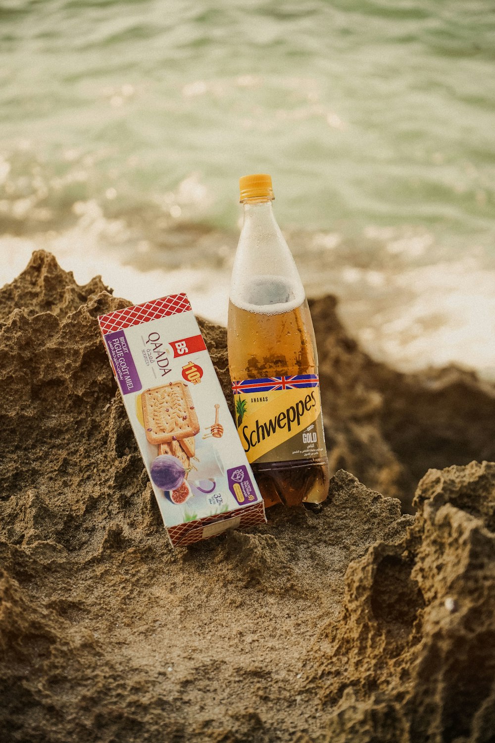 a bottle of wine sitting on top of a beach next to a package of crack