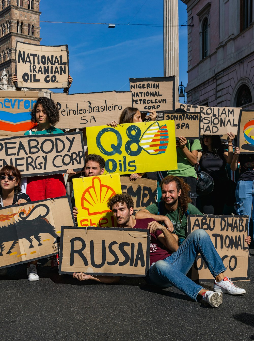 a group of people sitting on the side of a road holding signs