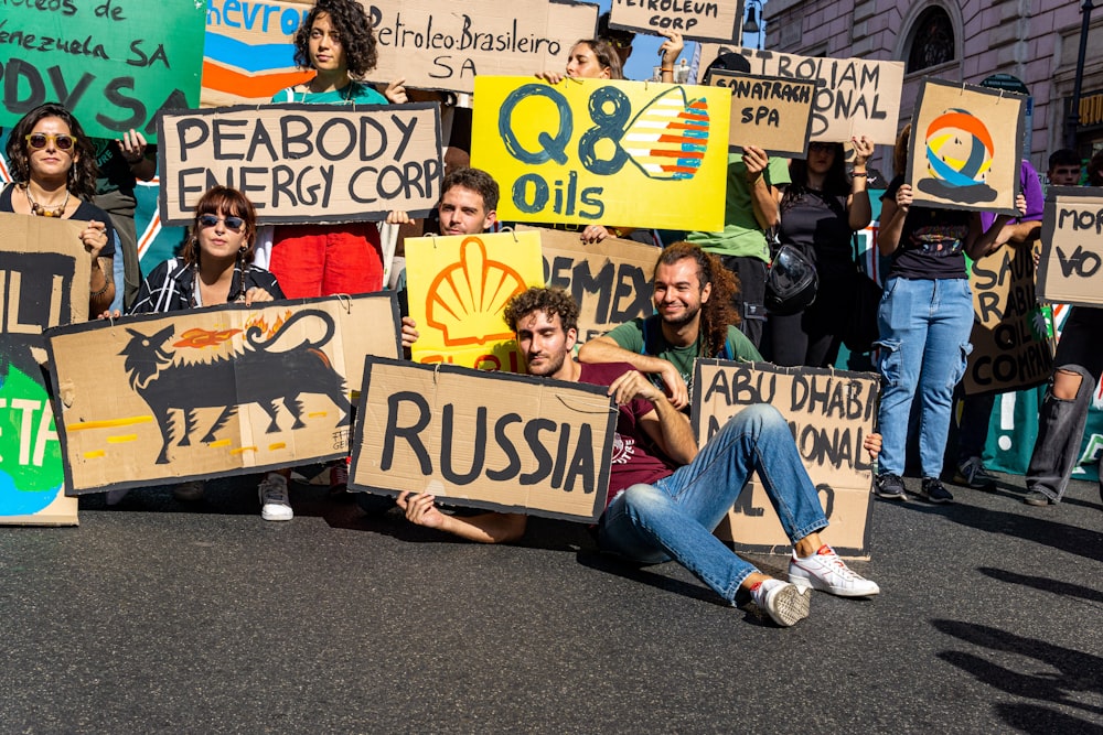 a group of people sitting on the street holding signs