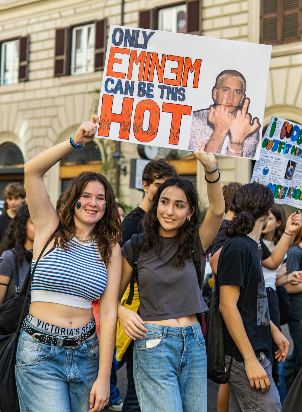 two women holding up a sign with a picture of a man on it