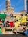 A group of people are gathered holding protest signs with names of various oil companies and countries, such as 'National Iranian Oil Co.', 'Nigerian National Petroleum Corp', 'Shell', and 'Russia'. The scene is set in an urban environment with historic architecture in the background. The individuals appear to be advocating for environmental issues related to fossil fuels.
