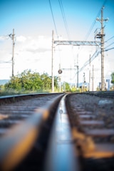 Steel rails being installed on a railway track under a clear sky.