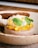 A beautifully plated dessert with a creamy base topped with citrus segments, fresh mint leaves, and delicate edible petals. A thin, crispy chocolate wafer is elegantly positioned on top, all set on a rustic ceramic plate.