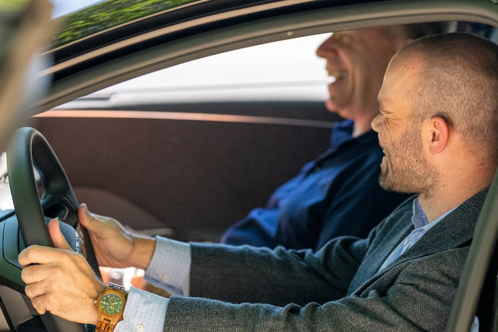 a man driving a car with another man behind him