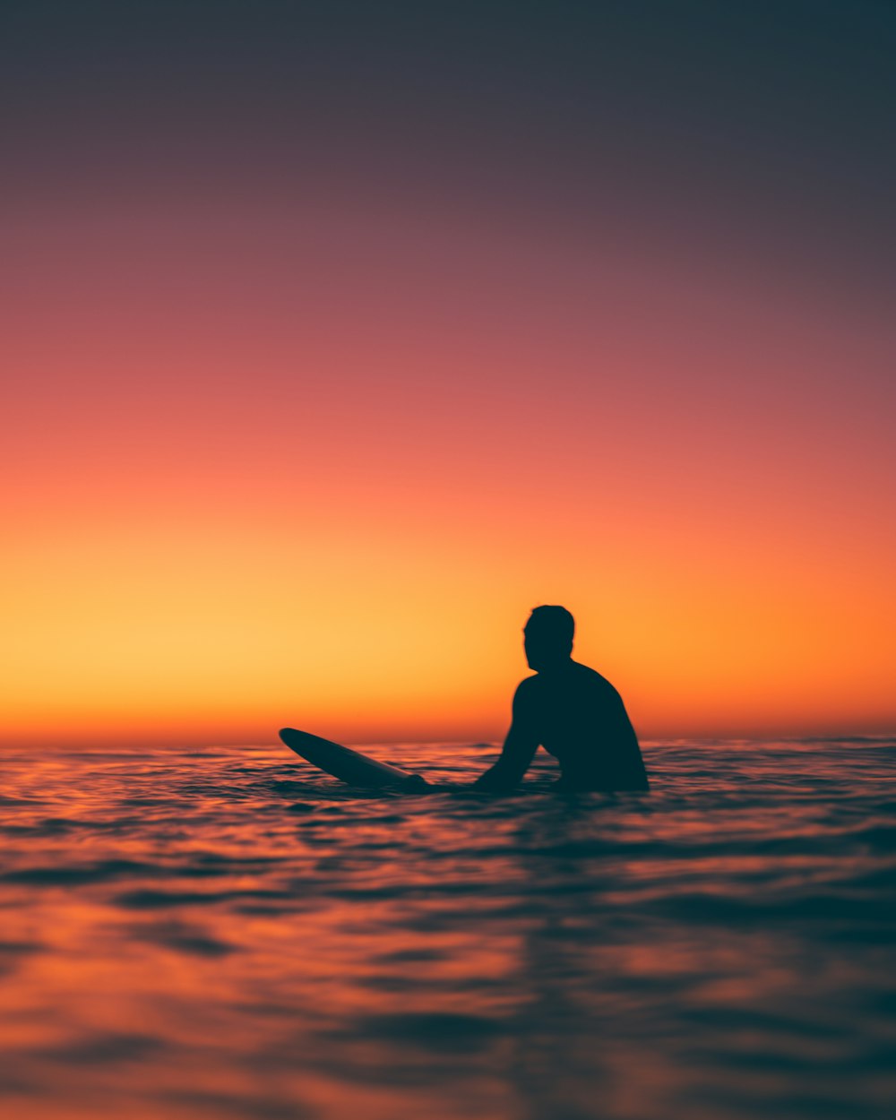 a man sitting on a surfboard in the ocean at sunset