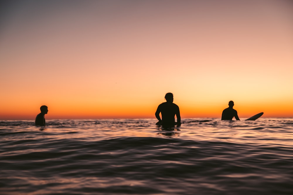 a group of people standing in the ocean at sunset