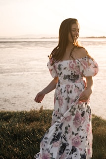 Close-up of a woman in a flowy tropical print dress walking along the shore at sunset.