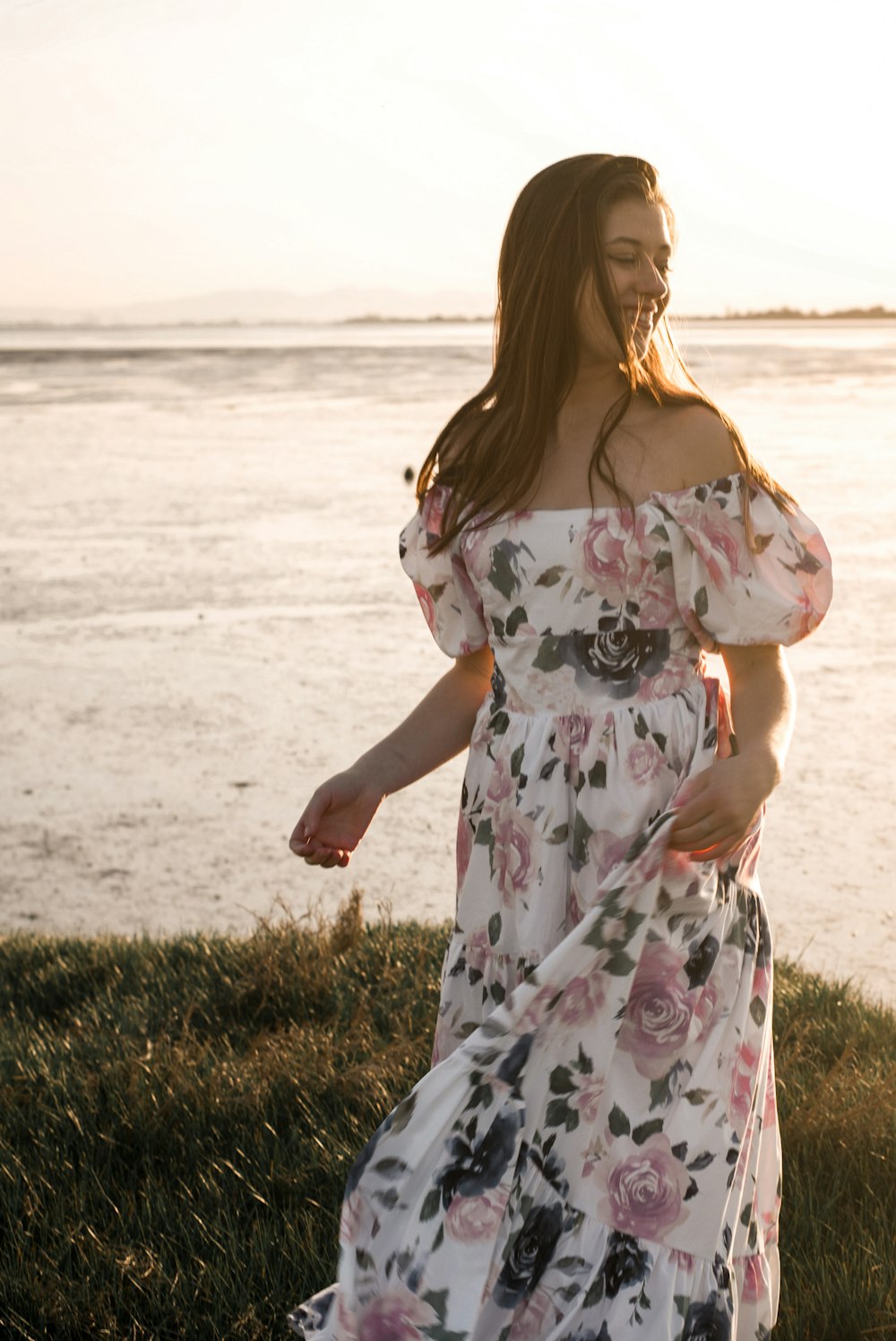 a pregnant woman in a floral dress standing by the water