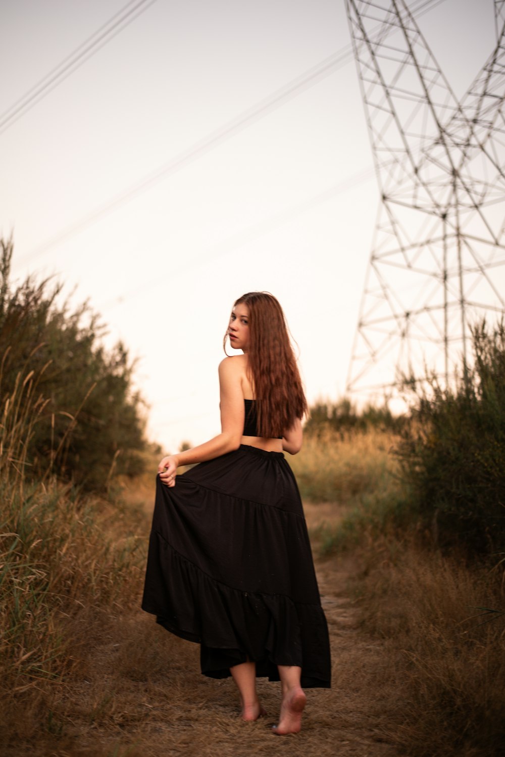 a woman in a black dress walking down a dirt road