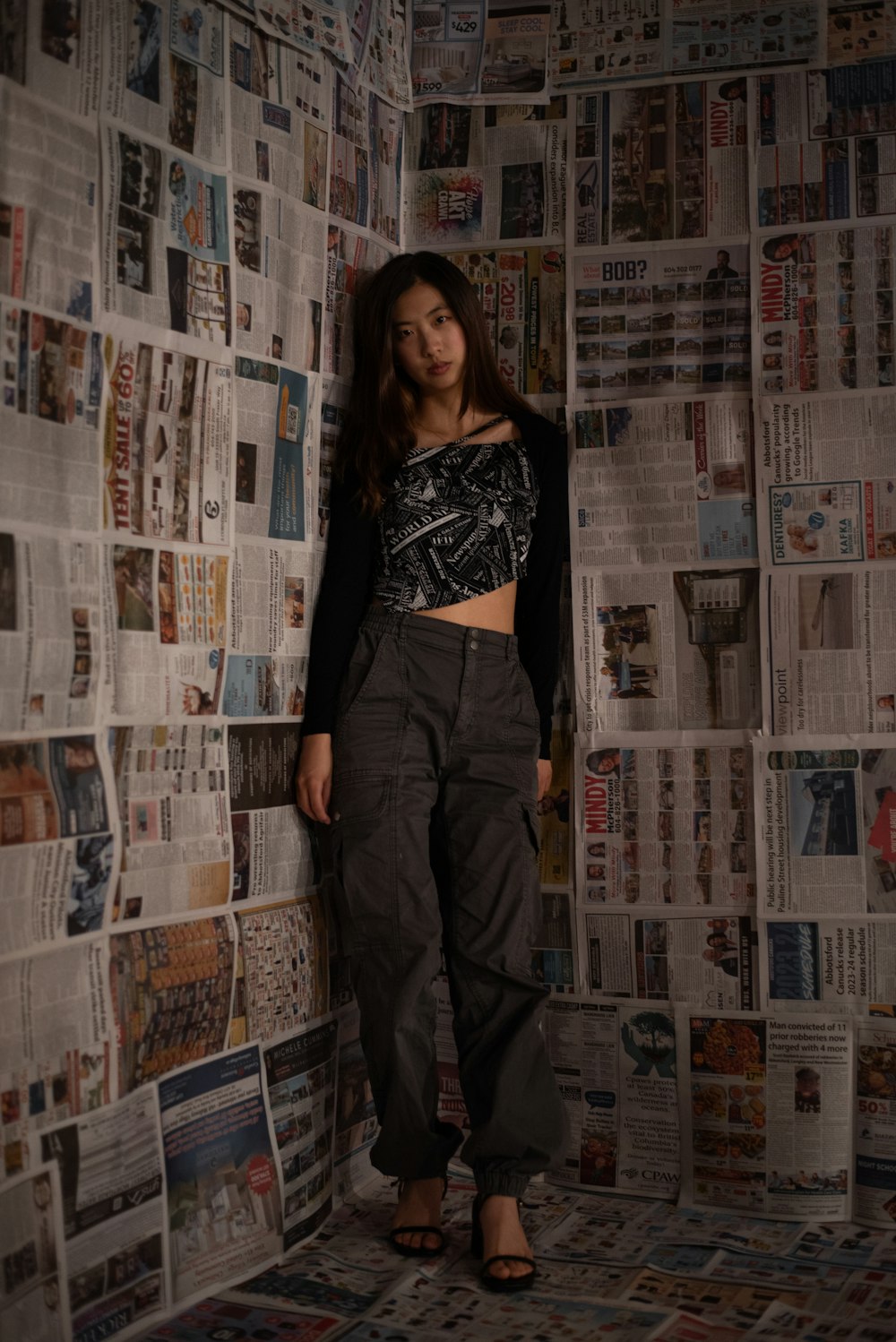 a woman standing in front of a wall covered in newspapers