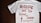 A white T-shirt with red text that reads 'Nothing but the blood of Jesus.' Below the main text, there is a smaller red biblical quote from Ephesians 1:7. The T-shirt is laid out flat on a dark wooden surface.