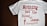 A white T-shirt with red text that reads 'Nothing but the blood of Jesus.' Below the main text, there is a smaller red biblical quote from Ephesians 1:7. The T-shirt is laid out flat on a dark wooden surface.