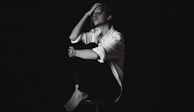 a black and white photo of a man sitting on a stool