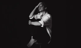 a black and white photo of a man sitting on a stool