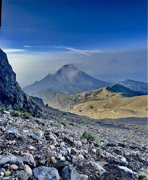 Runner navigating rocky terrain with the volcano in the background under a clear blue sky.