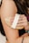 A hand holding a wooden massage brush with a fabric strap. The focus is on the brush being used on an arm. The person is wearing a black top, and there is a tattoo visible on the forearm, along with a ring on the finger.