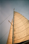 Detail of a sailboat’s rigging against a backdrop of soft white clouds and blue horizon