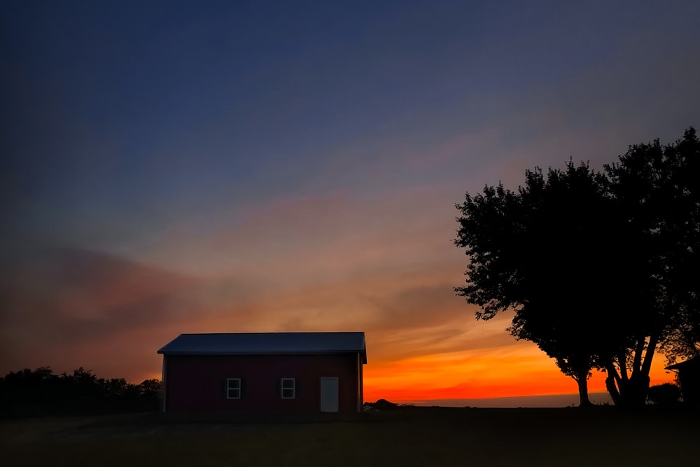 a red house sitting next to a tree at sunset