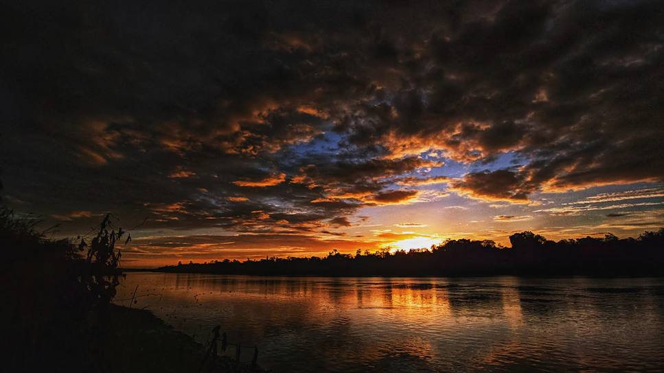 A vibrant sunset over the Tocantins river, with warm orange and purple hues reflecting on the water.