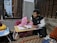 A warm, inviting classroom setting with a female teacher guiding a young boy in Quran recitation.