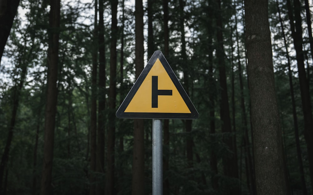 a yellow and black triangular sign sitting in the middle of a forest