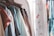 A collection of clothes hanging on a rack next to a white curtain with floral embroidery. The clothes are of various colors, including shirts and jackets, and hangers of different colors are visible. Next to the clothes, lanyards with text are hanging, adding a splash of color.