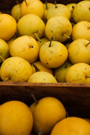 A close-up view of a collection of round, yellow Asian pears with visible speckles and stem ends, arranged tightly in a wooden crate.