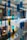 Colored glass panels or hanging decorative pieces in various shapes and hues of blue, green, and yellow are suspended in an indoor setting with a blurred background of lights, plants, and modern architectural elements.