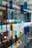 Colored glass panels or hanging decorative pieces in various shapes and hues of blue, green, and yellow are suspended in an indoor setting with a blurred background of lights, plants, and modern architectural elements.